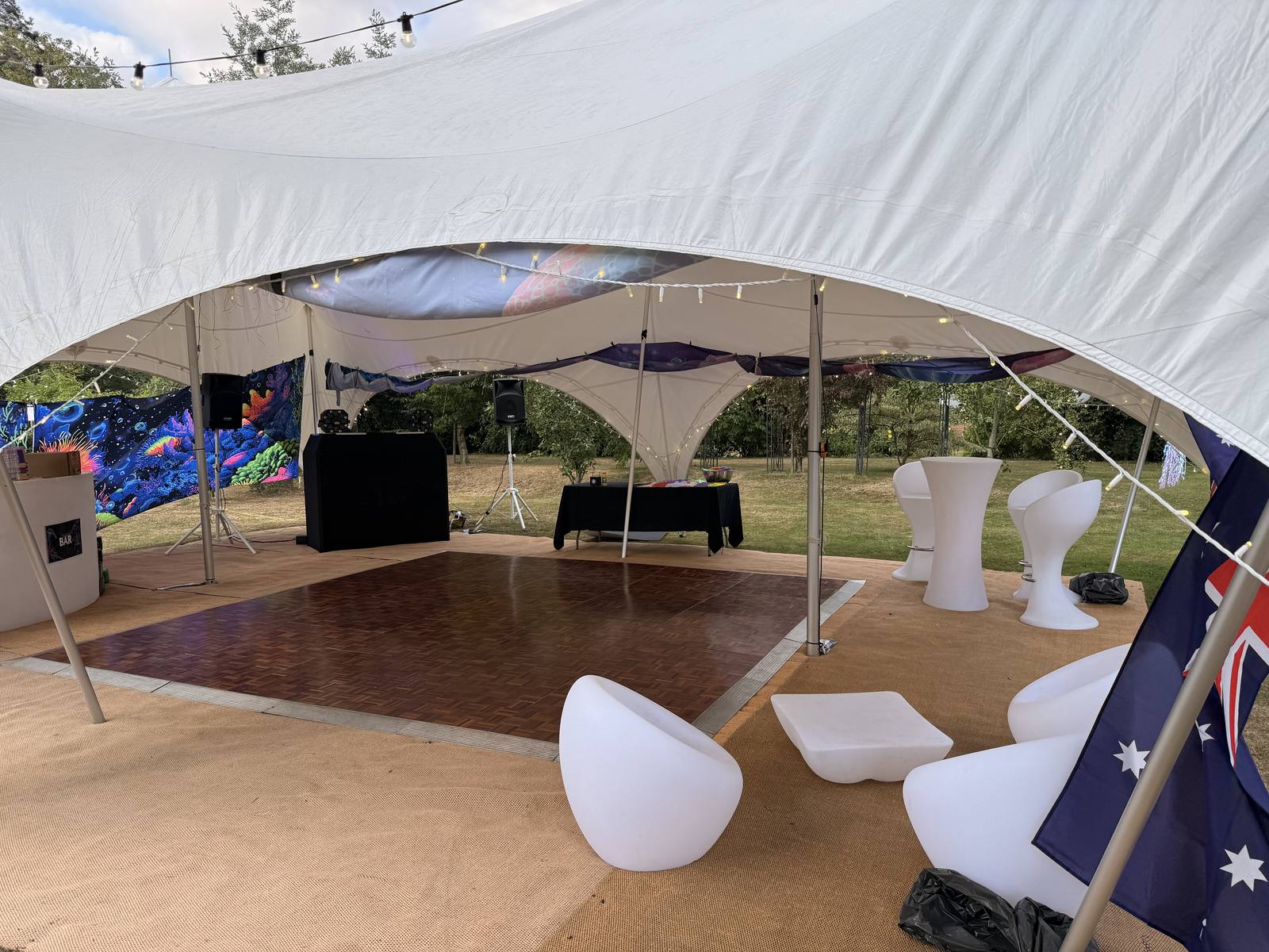 Parquet dancefloor set up at an outdoor event with DJ booth, bar and lounge seating under festoon lighting